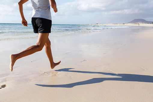 Fit Asian runner jogging on beach barefoot