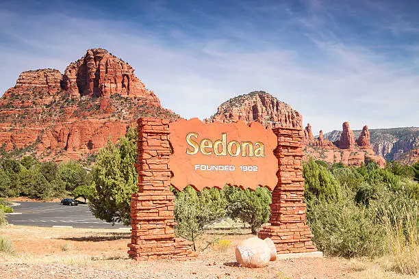 A public sign welcoming visitors to Sedona with the famous red rocks in the background.