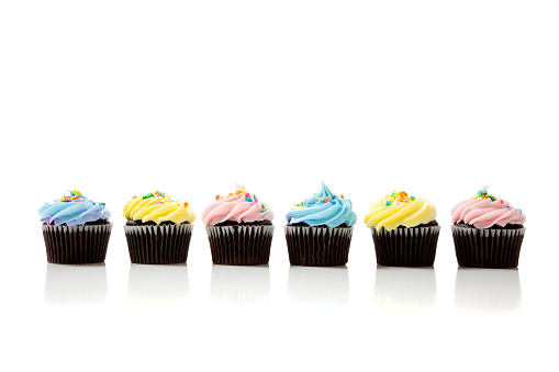 Pastel cupcakes including blue, pink and yellow on a white background with copy space