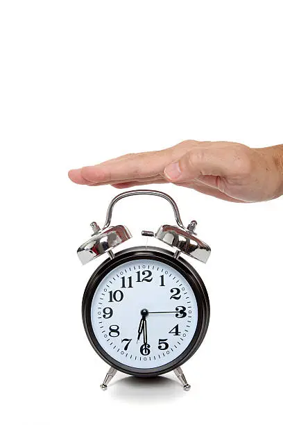 A hand reaching for an old-fashioned alarm clock on a white background