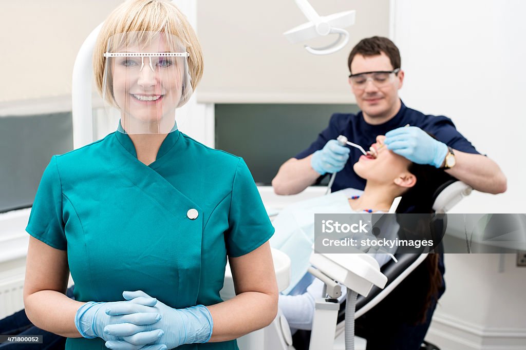 Male dentist treat patient in clinic. Assistant posing, dentist treating  patient behind 2015 Stock Photo