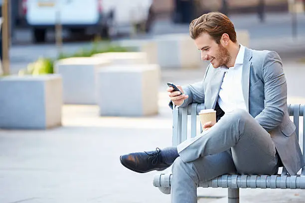 Photo of Businessman On Park Bench With Coffee Using Mobile Phone