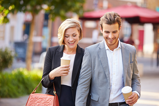 Business Couple Walking Through Park With Takeaway Coffee