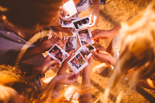 High angle shot of teen friends sharing instant photos of themselves having fun outdoors