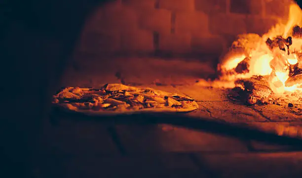 Freshly made pizza being placed carefully inside a traditional wood fire oven