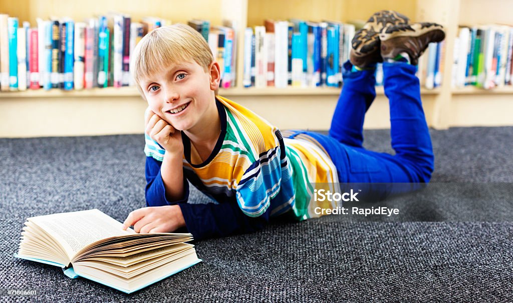 Feliz junior bookworm sonrisas, lying on library piso de lectura - Foto de stock de 10-11 años libre de derechos