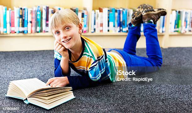Feliz Junior Bookworm Sonrisas Lying On Library Piso De Lectura Foto de stock y más banco de imágenes de 10-11 años