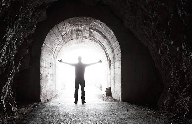 istock Man stands in dark tunnel with glowing end 471808675