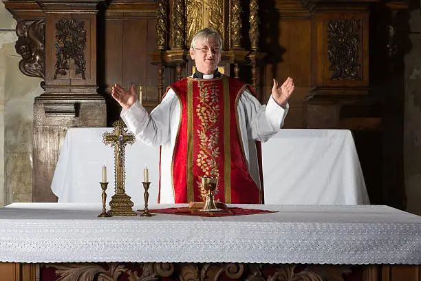 Christian priest blessing the hosts and chalice in a 17th century church interior