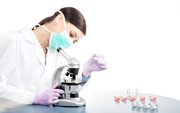 Woman in mask using pipette and microscope. stock photo