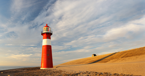 A bright red lighthouse illuminated by the setting sun. Location: Zeeland, Netherlands. Seamlessly stitched panorama out of 5 images. Much copy space.