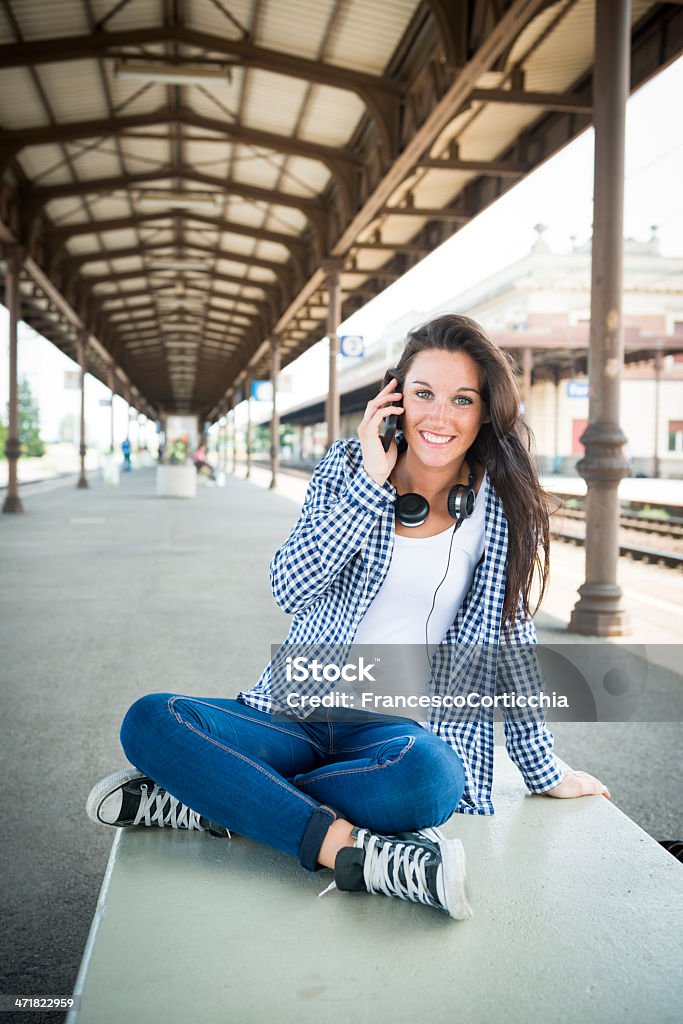 Giovane donna felice con smartphone alla stazione ferroviaria - Foto stock royalty-free di Abbigliamento casual
