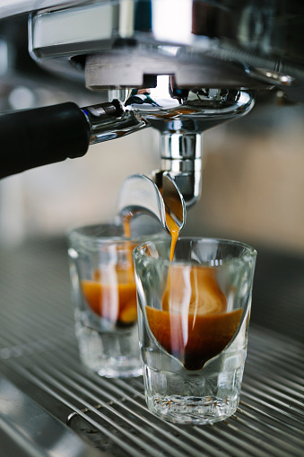 A close up shot of hot coffee dripping out of the portafilter of a professional espresso machine into  small espresso shots.