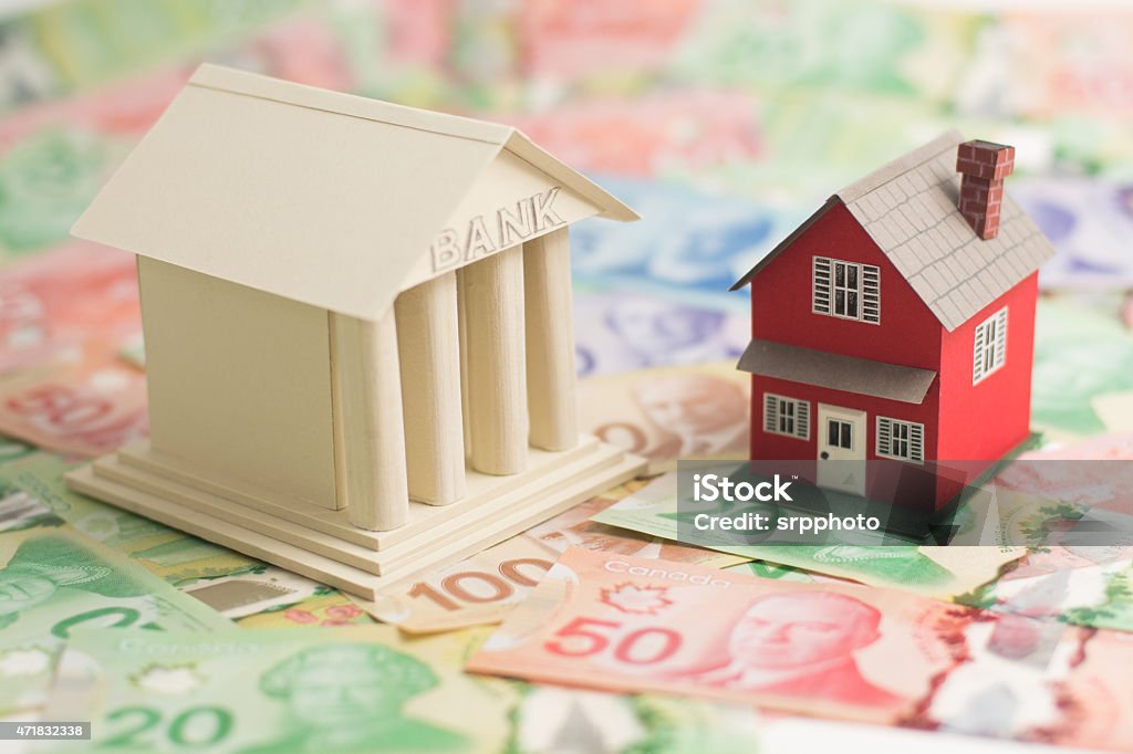 Canadian housing market bank and little house sitting on Canadian money.  Bank - Financial Building Stock Photo