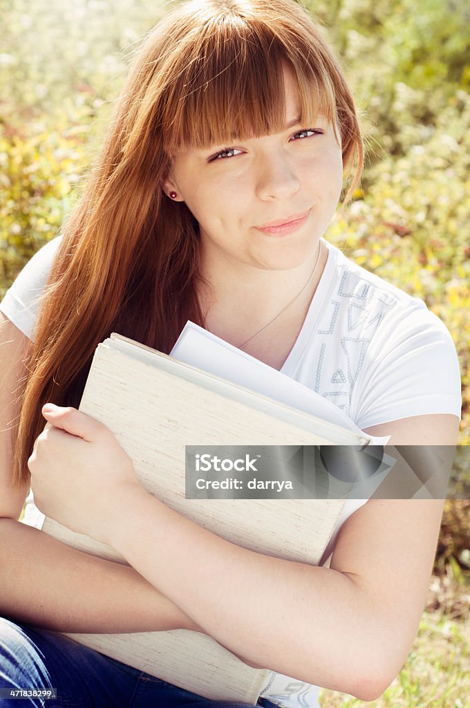 Female Student Portrait Portrait of a happy female student sitting casually on the street, holding a book to study. 20-29 Years Stock Photo