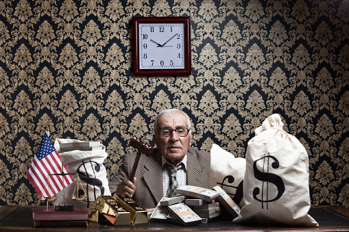 Senior man posing with stack of dollar bills, US constitution, gavel , scales of justice and money bag for inequality of income