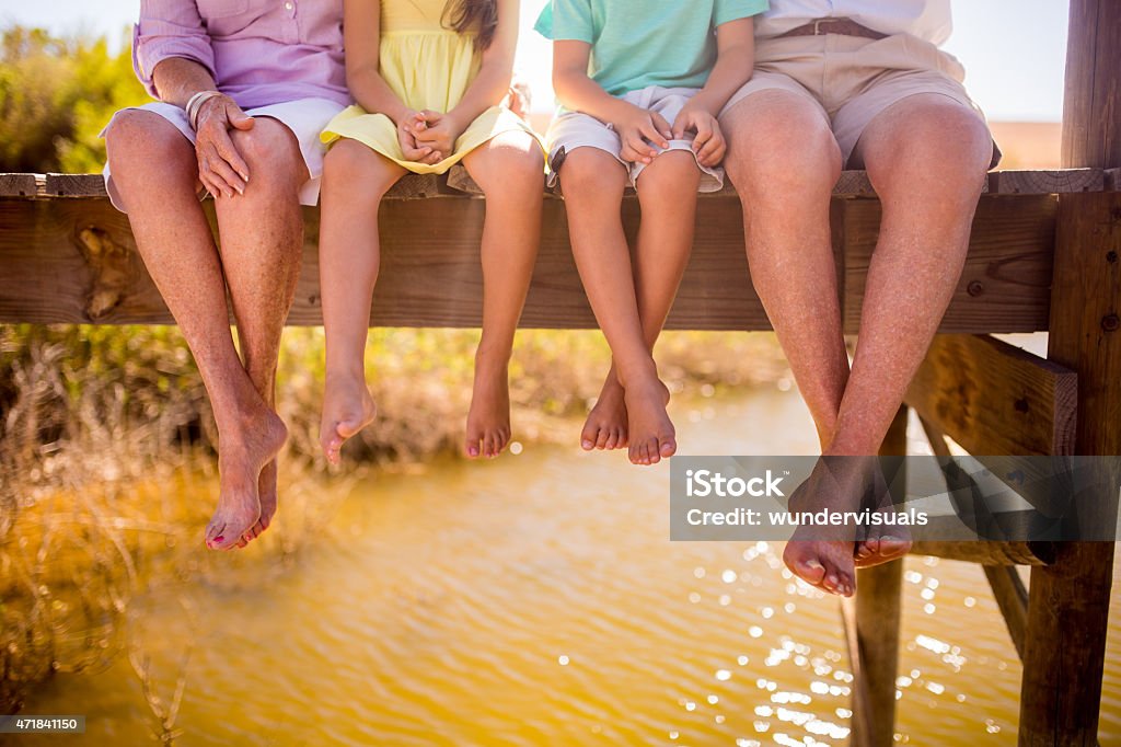 Grandparents and grandchildren sitting together on a jetty Cropped image of the legs of grandparents and grandchildren dangling their legs off a jetty while sitting alongside each other Family Stock Photo