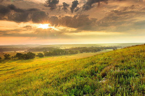 A light fog and heavy dew fills the valley as this warm sunrise warms the sky on a mild summer morning in the Kansas Tallgrass Prairie Preserve.