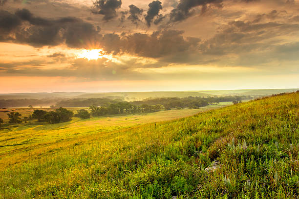 Dramatic Sunrise over the Kansas Tallgrass Prairie Preserve National Park A light fog and heavy dew fills the valley as this warm sunrise warms the sky on a mild summer morning in the Kansas Tallgrass Prairie Preserve. kansas stock pictures, royalty-free photos & images