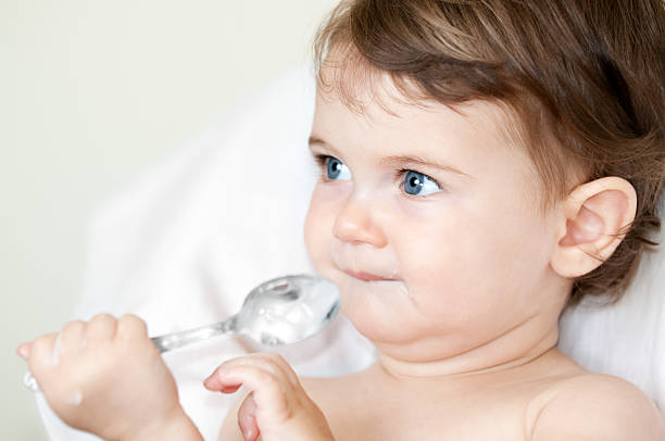 Baby girl holding a dirty spoon of yogurt.