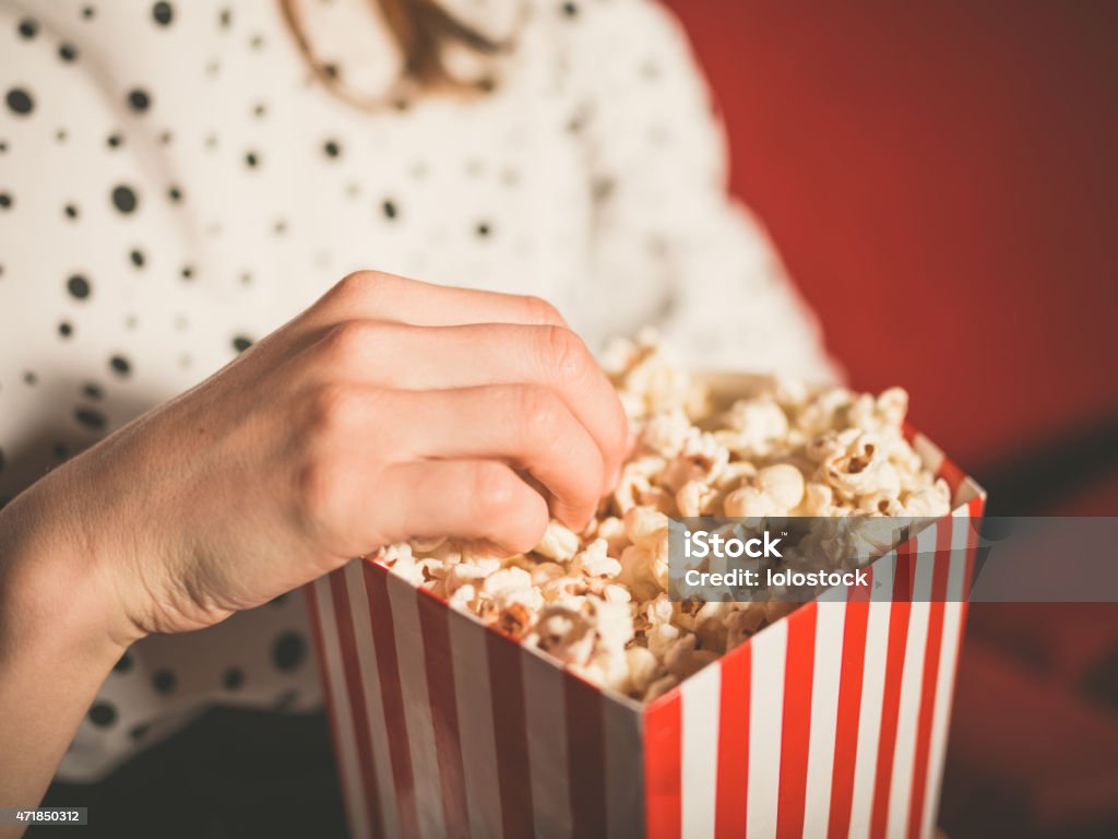 Young Woman Eating Popcorn in Movie Theater Closeup on a young woman eating popcorn in a movie theater Popcorn Stock Photo