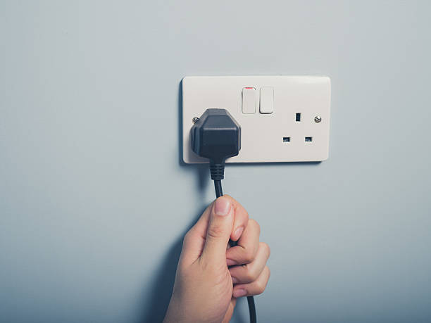 istock Male hand pulling a black cord from a white outlet 471851116