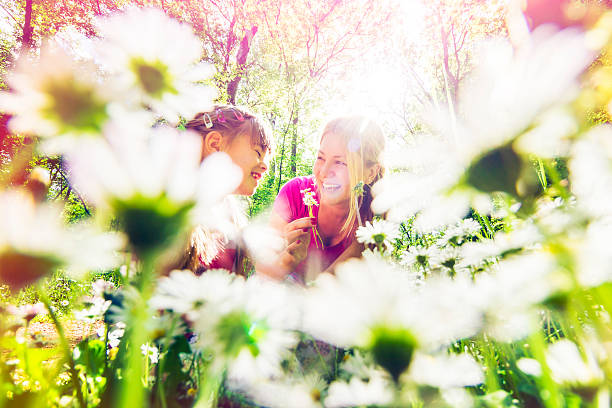 Loving mother and daughter are picking daisies and having fun in meadow in spring. An ants view, surface level. Toned image, AdobeRGB profile.