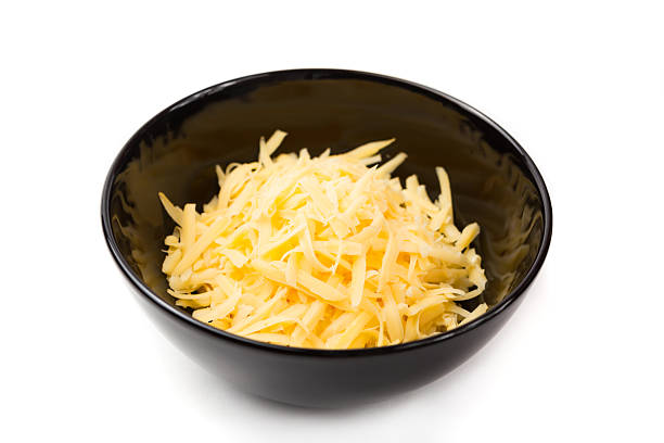A black bowl of grated cheddar cheese Grated cheddar cheese in a black bowl, isolated on white. shredded mozzarella stock pictures, royalty-free photos & images