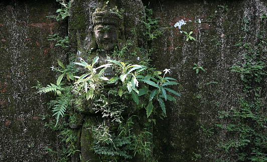 Hindu god statue covered by grass and moss in Ubud Bali Indonesia