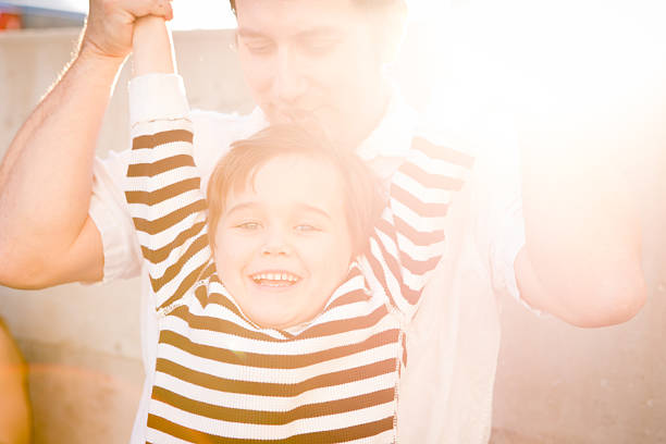 счастливый отец держит вверх маленький сын за пределами в солнечный день - brown hair caucasian little boys men стоковые фото и изображения