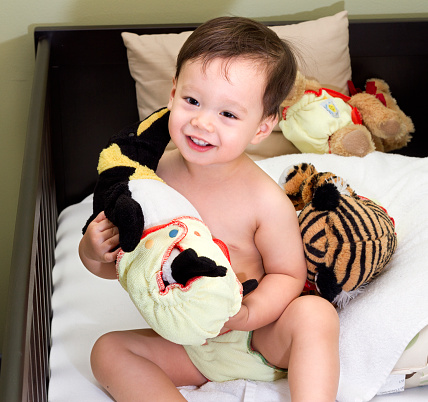A toddler boy holding his plush toys and they're all wearing cloth diapers.