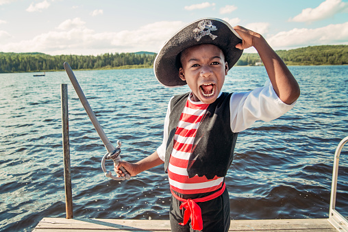 Portrait of very expressive little african-american boy costumed as a pirate on a lake outside. Copy space.