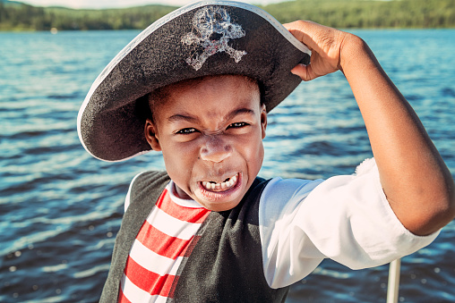 Portrait of very expressive little african-american boy costumed as a pirate on a lake outside. 