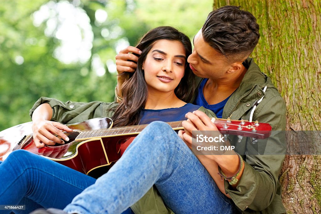 Amorevole giovane coppia seduta sotto un albero con chitarra - Foto stock royalty-free di 20-24 anni