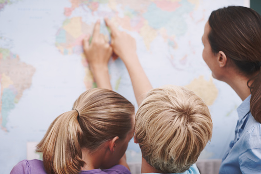 Two excited schoolchildren pointing at a world map as their teacher looks on