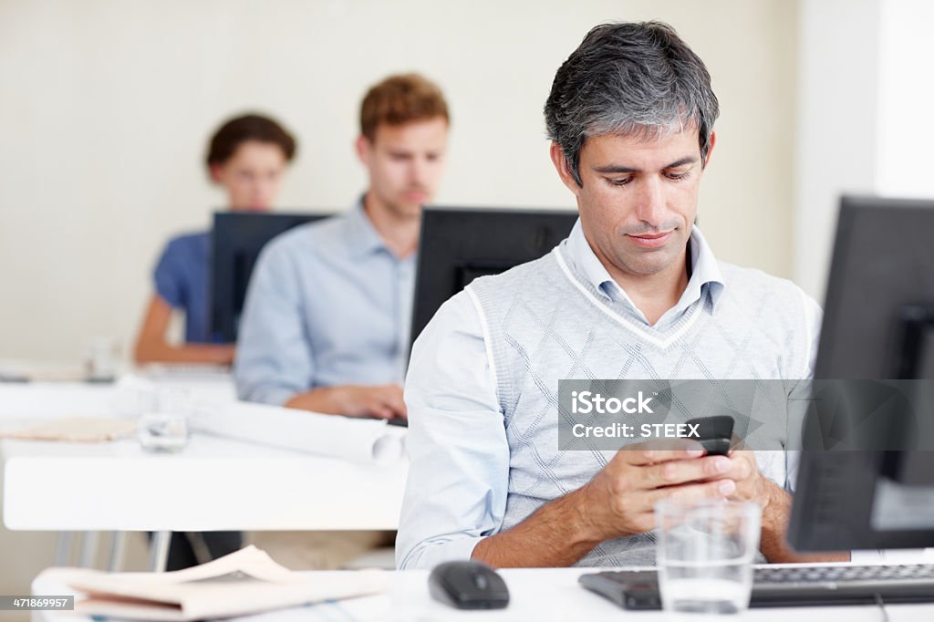 Getting distracted at work? Shot of an office worker sending a text message while sitting at his workstation with coworkers behind him 30-39 Years Stock Photo