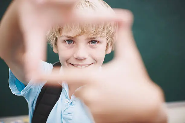 A young boy framing you with his fingers in the classroom