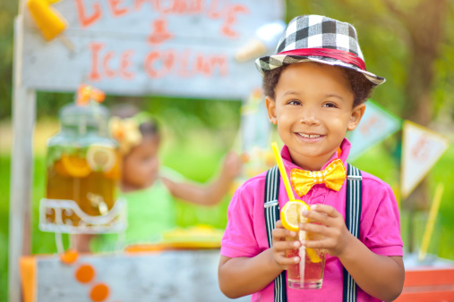 Little boy standing near a lemonade stand outdoors in summer 
