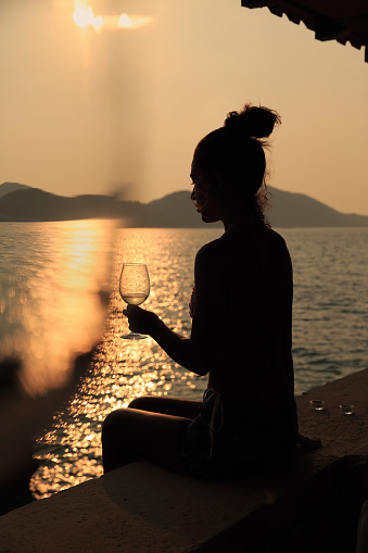 Beautiful woman drinking a glass of white wine,  at sunset.
