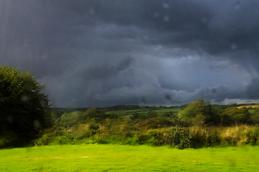 Dramatic early Autumn landscape seen through a rain smeared window. Black storm clouds and very heavy rain with sunlight slanting in. Cornwall UK. Autumn 2013.
