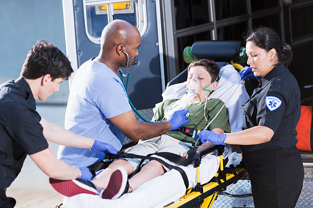 Doctor and paramedics helping child Multi-ethnic doctor and paramedics (30s, 40s) helping boy (12 years) lying on a stretcher outside an ambulance. stretcher stock pictures, royalty-free photos & images