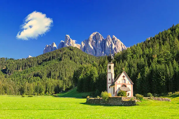 The church St. Johann in Ranui in the Villnoess / Funes valley in the Dolomites, South Tyrol, Italy. In the background the Geisler Group mountain range. Warm evening light.