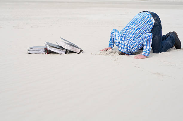 office worker hiding head in sand stock photo