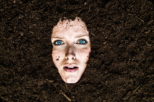 Woman is covered in dirt and only her face is visible. She is looking at the camera and looks a bit shocked.
