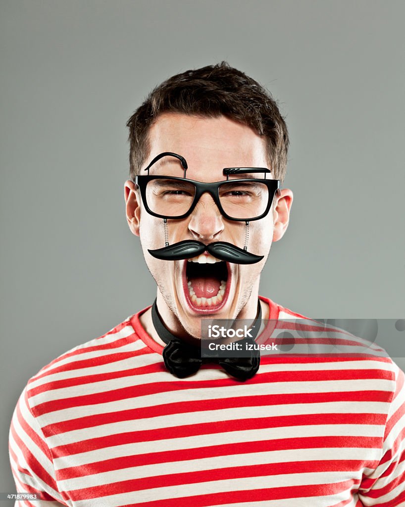 Anger Portrait of angry young man wearing fake mask screaming at the camera. Studio shot, gray background. 20-24 Years Stock Photo