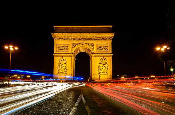 The Arc de Triomphe in Paris, France at night. A long exposure captures the car lights as they approach and go around the monument.