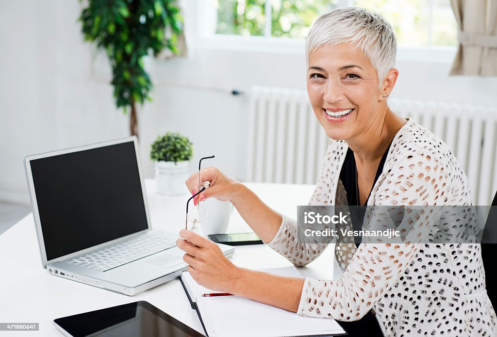 Mature business woman Beautiful cheerful mature woman at office holding glasses, smiling and looking at camera Senior Women Stock Photo