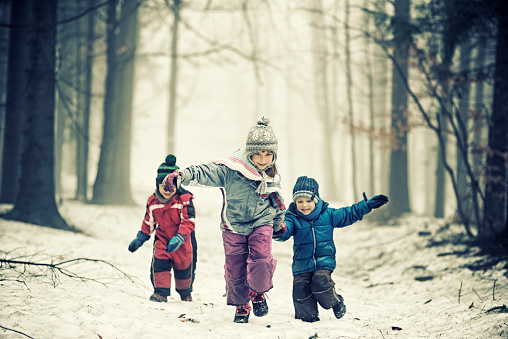Three happy kids running in cold misty winter forest.