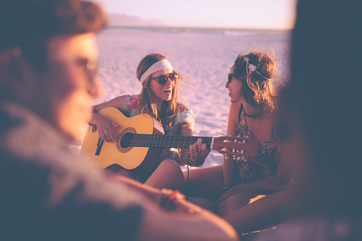 Girl playing guitar and singing for her friends at a summer evening beachparty