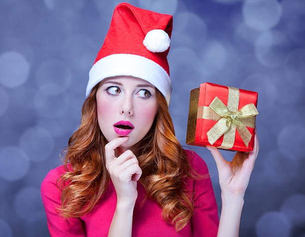 istock Redhead girl in christmas hat with gift. 471883571